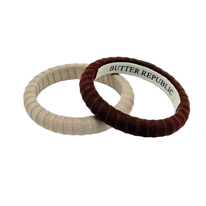 two suede Butter Republic bracelets, one beige and one brown, with logo brand label on the bracelet interior