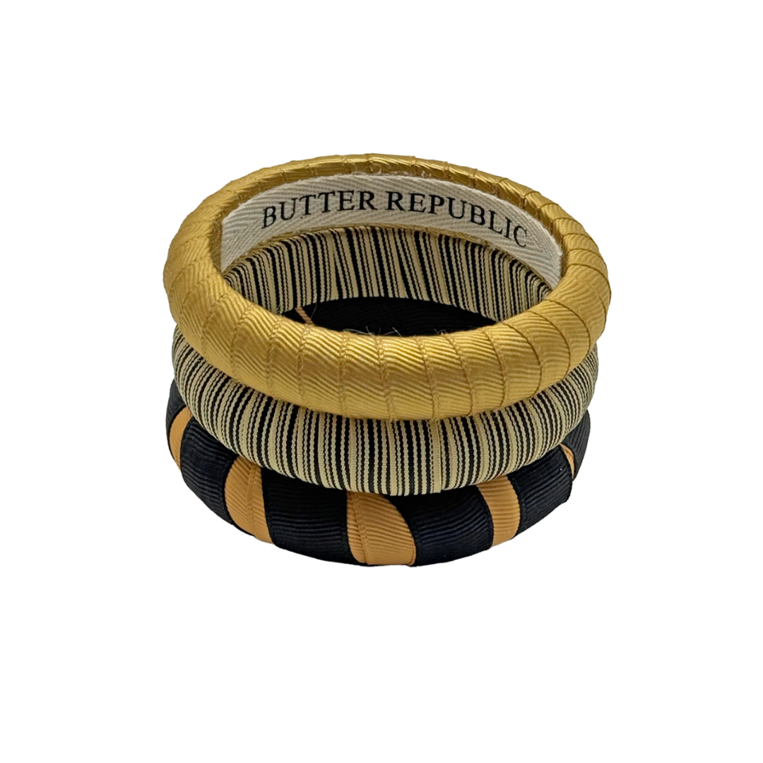 three black and gold Butter Republic bracelets stacked, with logo brand label on the bracelet interior