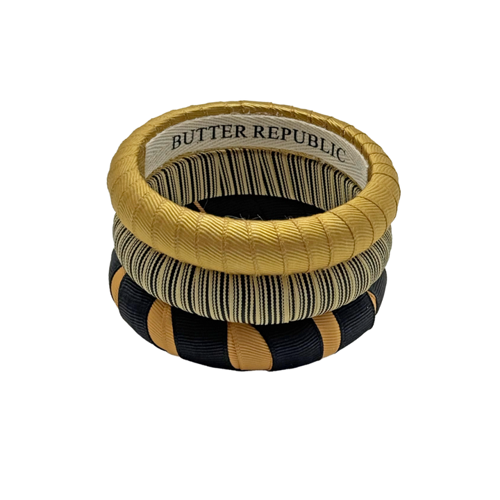 three black and gold Butter Republic bracelets stacked, with logo brand label on the bracelet interior
