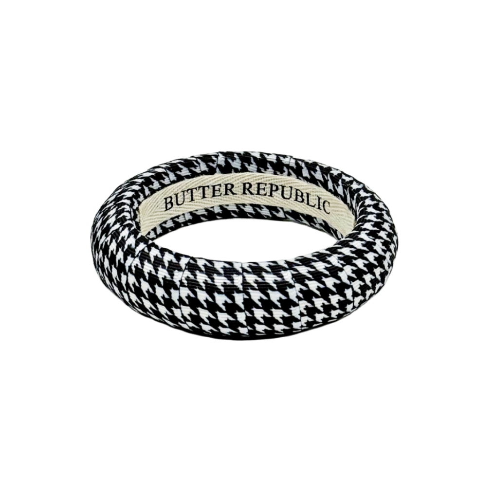 A houndstooth patterned bangle bracelet with a cream-colored inner band featuring the &