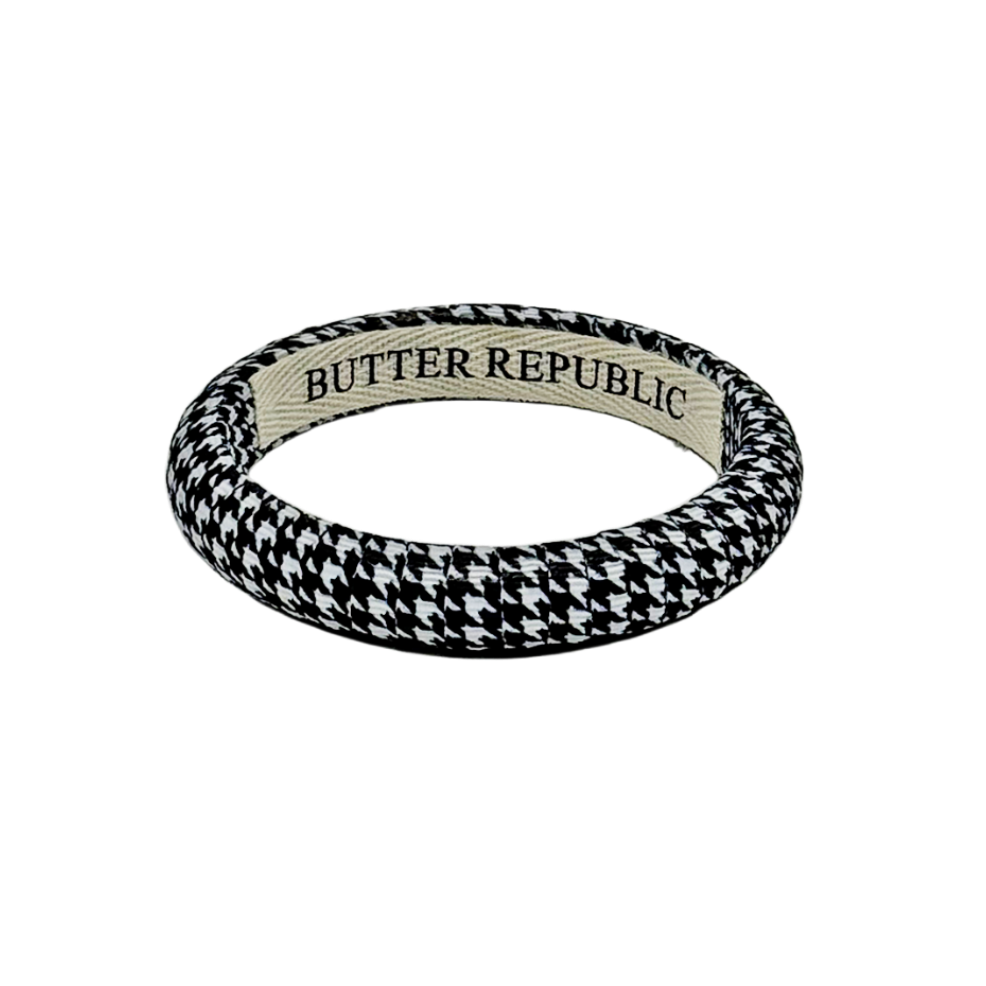 a black and white houndstooth patterned bangle bracelet with Butter Republic brand label on the interior