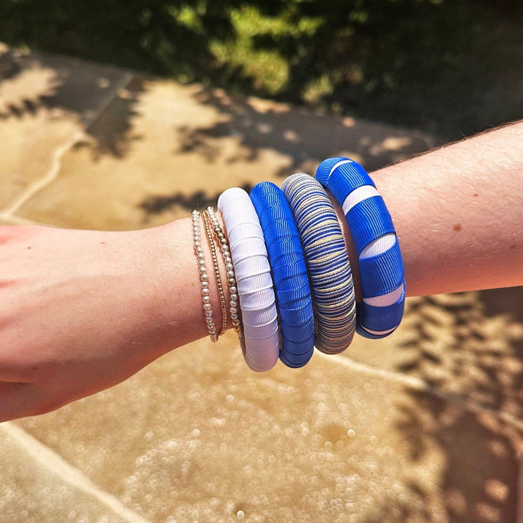 Woman wearing multiple blue and white Butter Republic bracelets on a stone surface with grass in the background