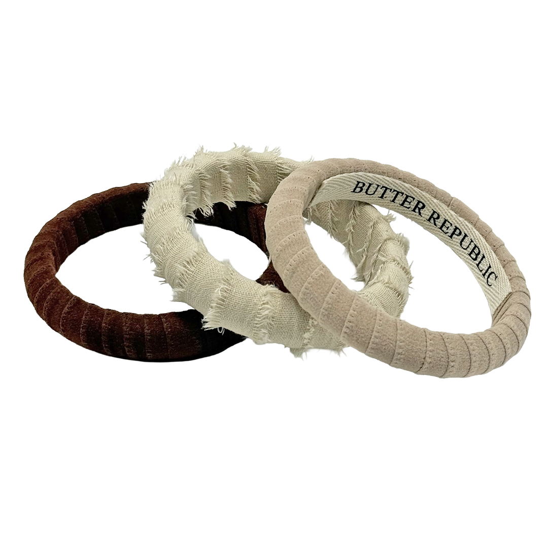 three Butter Republic bracelets of various textures in brown, natural, and beige with logo brand label on the interior of the bracelet