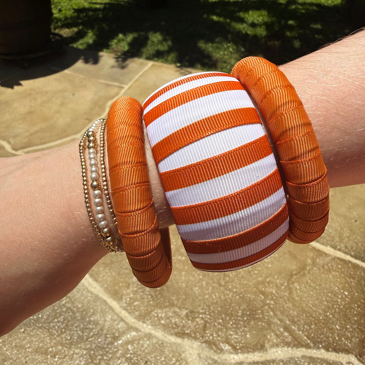 Close-up of a wrist wearing burnt orange bracelets on a stone surface with grass in the background