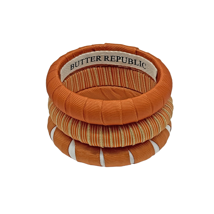 stack of three burnt orange, cream, and white Butter Republic bracelets with logo brand label on the interior of the bracelet