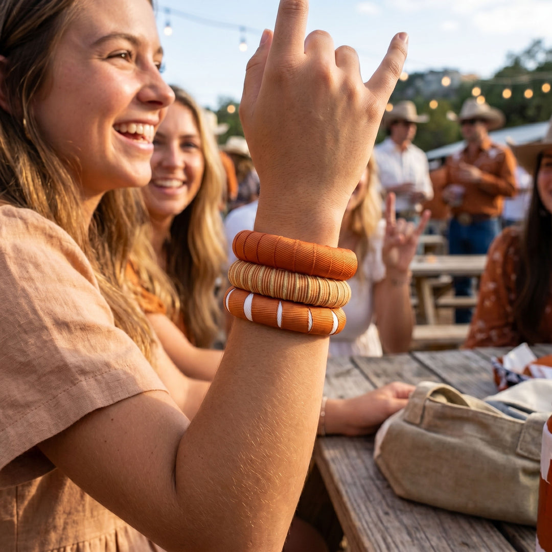 Woman with multiple burnt orange Butter Republic bracelets at an outdoor event