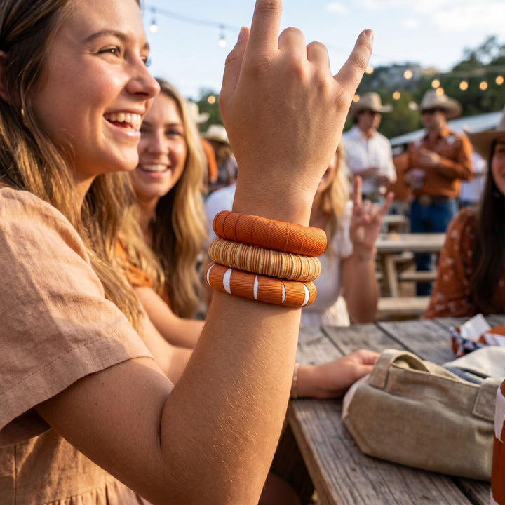 Woman with multiple burnt orange Butter Republic bracelets at an outdoor event