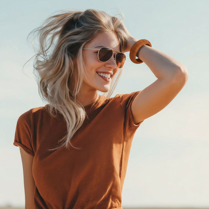 woman wearing a burnt orange Butter Republic bracelet, burnt orange t-shirt, and black aviator sunglasses