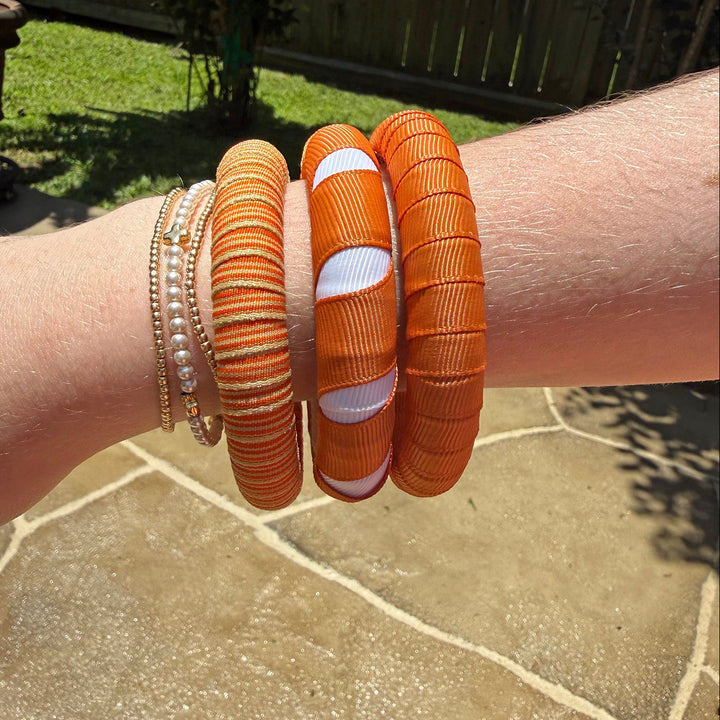 Close-up of a wrist wearing multiple burnt orange Butter Republic bracelets on a stone patio.