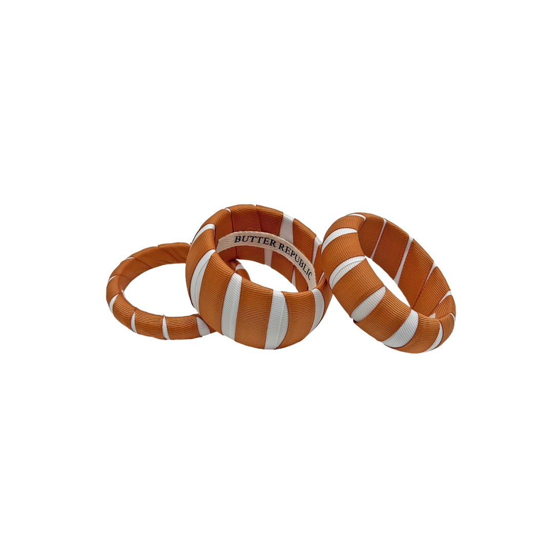 three burnt orange and white multi-width Butter Republic bracelets with brand logo label on the interior of the bracelet