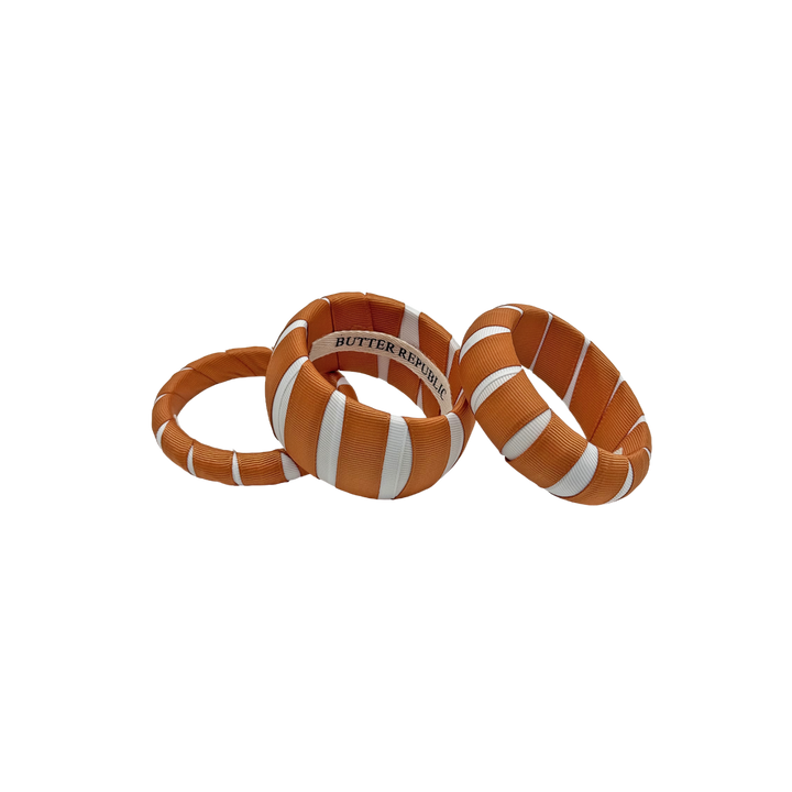 three burnt orange and white multi-width Butter Republic bracelets with brand logo label on the interior of the bracelet