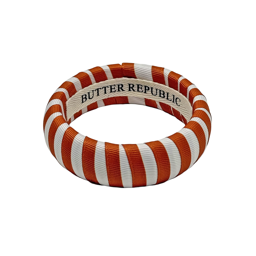 burnt orange and white striped Butter Republic bracelet with logo brand label on the interior of the bracelet