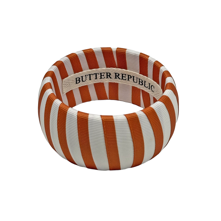 burnt orange and white striped Butter Republic bracelet with logo brand label on the interior of the bracelet