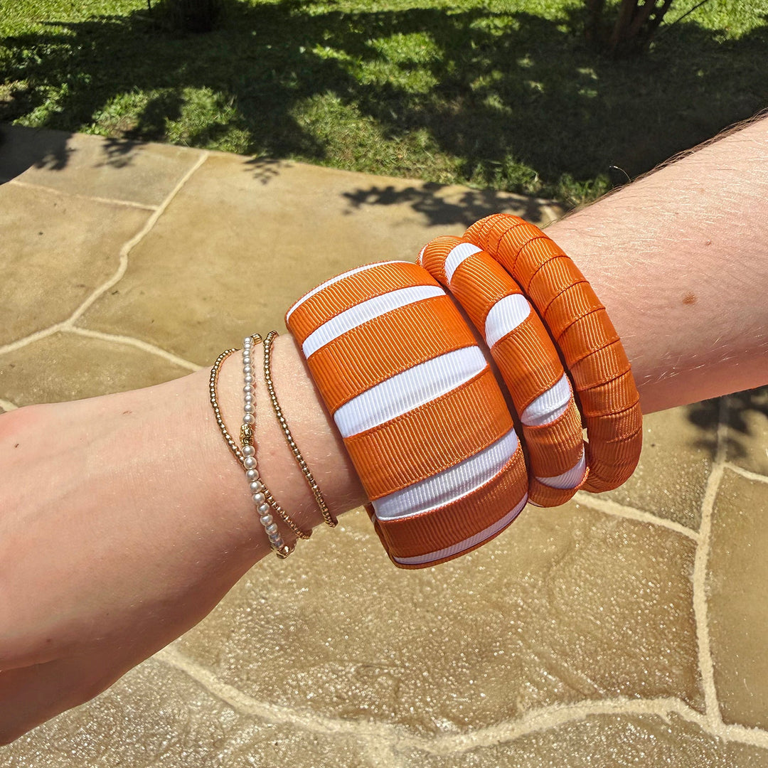 three burnt orange and white Butter Republic bracelets with a tile and grass background