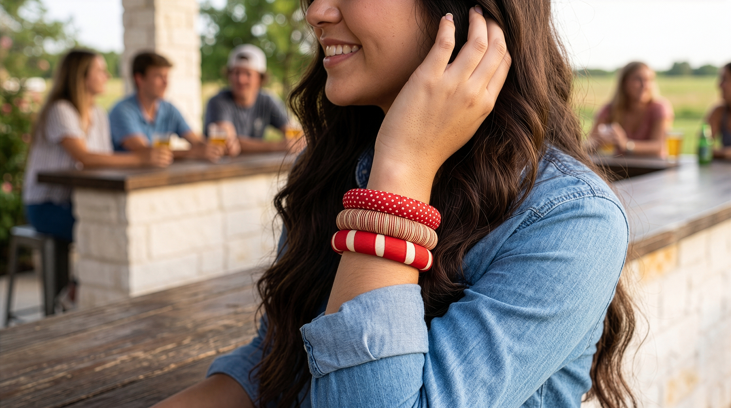 woman outdoors wearing three crimson and cream Butter Republic bracelets, with multiple young college-aged men and women blurry behind her