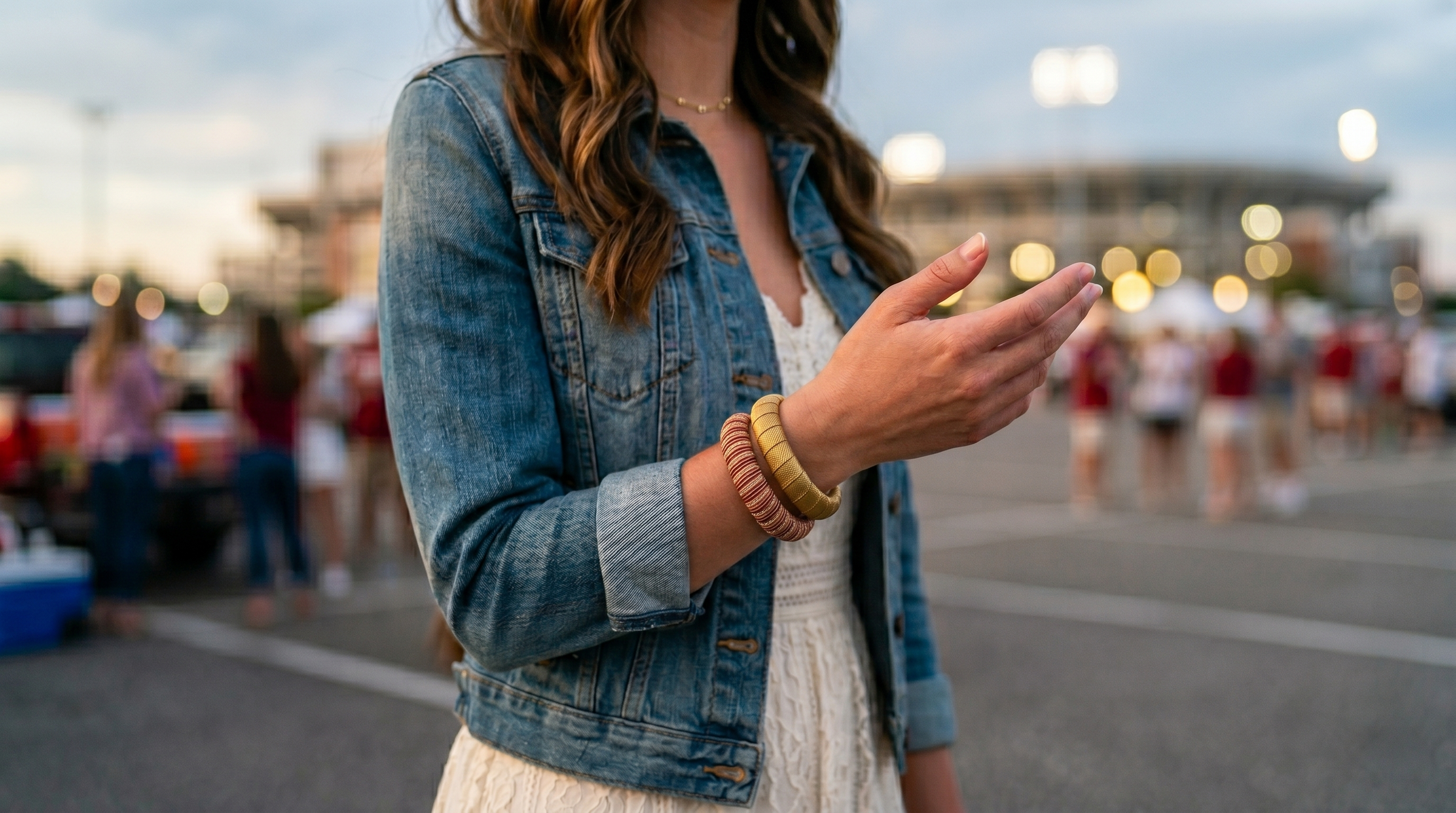 woman wearing gold and crimson Butter Republic bracelets and a denim jacket with blurred background of people and lights