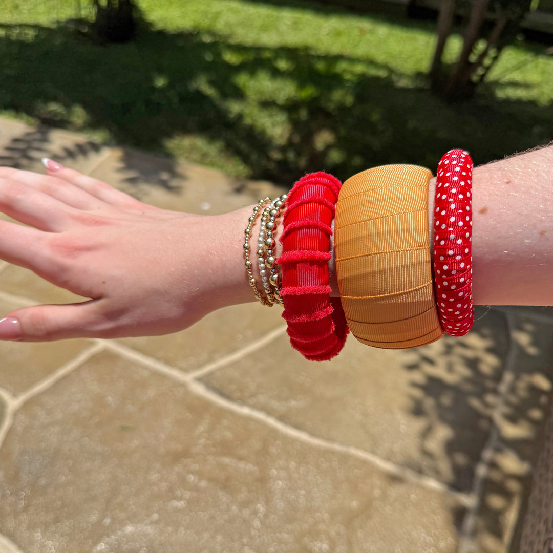 Woman wearing multiple gold and red Butter Republic bracelets on a stone patio with grass and wooden fence in the background