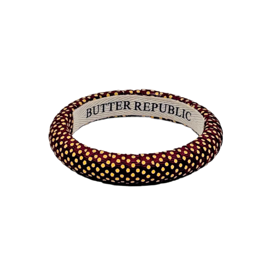 A Butter Republic bangle bracelet featuring garnet and gold polka dots, with the brand name printed on the inner band.