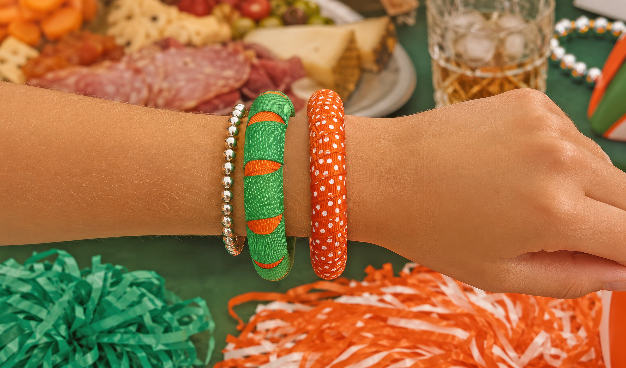 A close-up of a woman's wrist wearing Butter Republic green and orange bangle bracelets