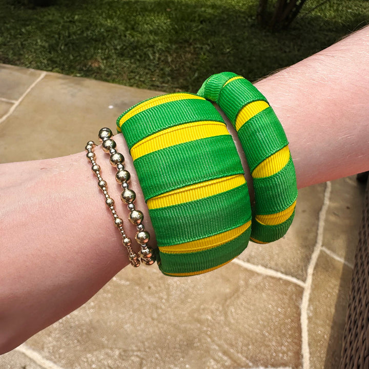 Woman wearing green and yellow Butter Republic bracelets on a stone surface with grass in the background