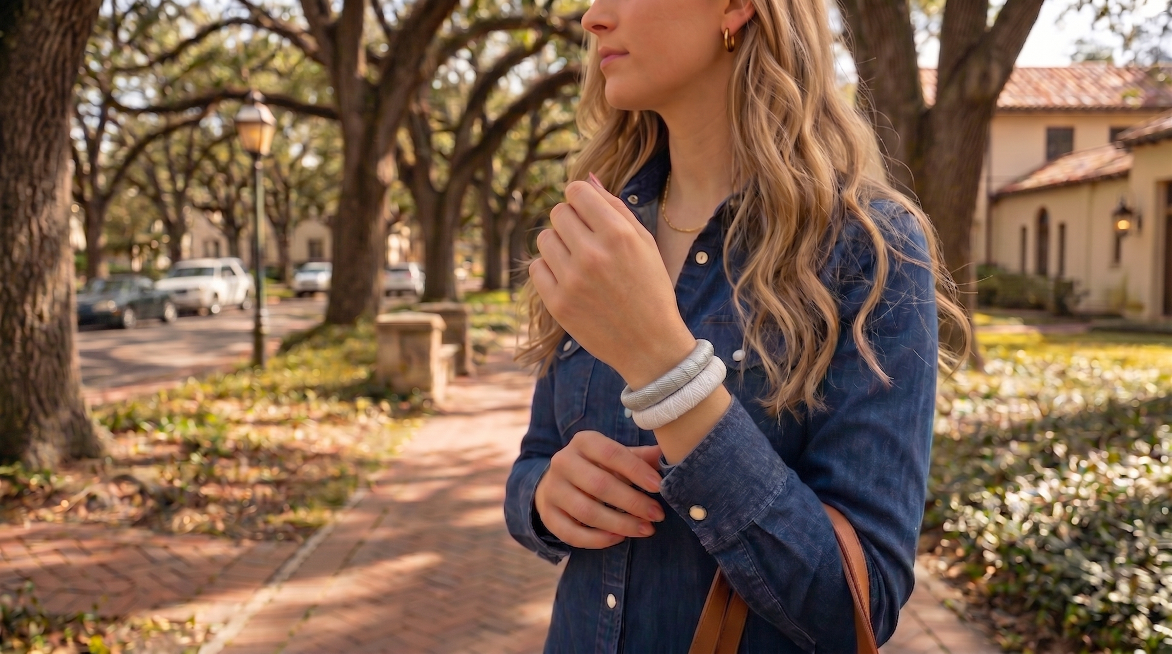 woman wearing a silver Butter Republic bracelet and a white Butter Republic bracelet, adjusting her denim jacket outdoors with trees and buildings in the background