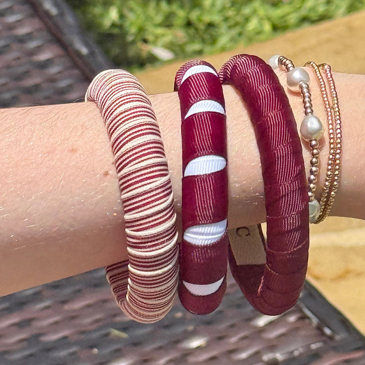 Close-up of a wrist wearing multiple maroon Butter Republic bracelets with a blurred outdoor background
