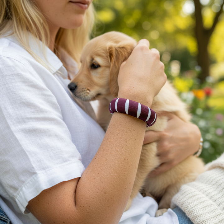 young woman wearing a Butter Republic maroon and white bracelet, holding a puppy outdoors with a blurred background