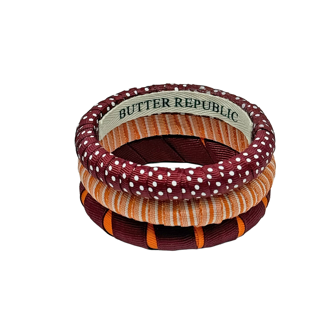 A stack of three assorted design maroon and orange Butter Republic bracelets