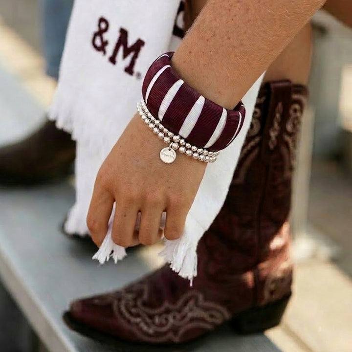 close-up of a young woman wearing a maroon and white Butter Republic bracelet with cowboy boots and a towel