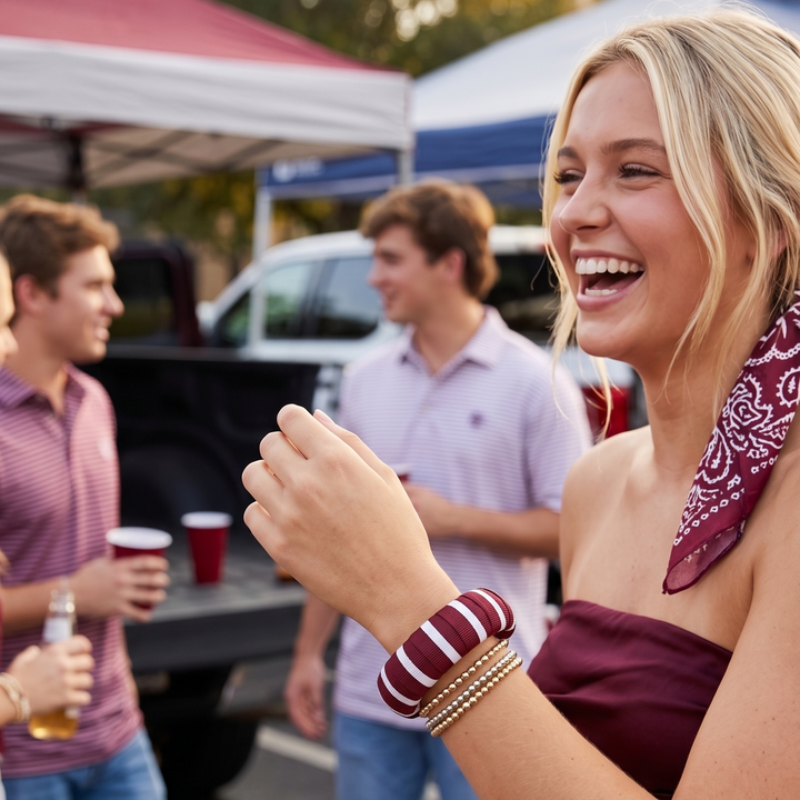 Woman with a wearing a maroon and white stripe Butter Republic bracelet laughing at an outdoor event with people and tents in the background