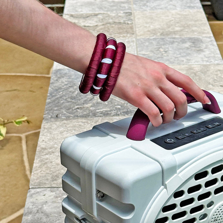Person wearing maroon and white Butter Republic bracelets, picking up a Turtlebox-type of speaker 
