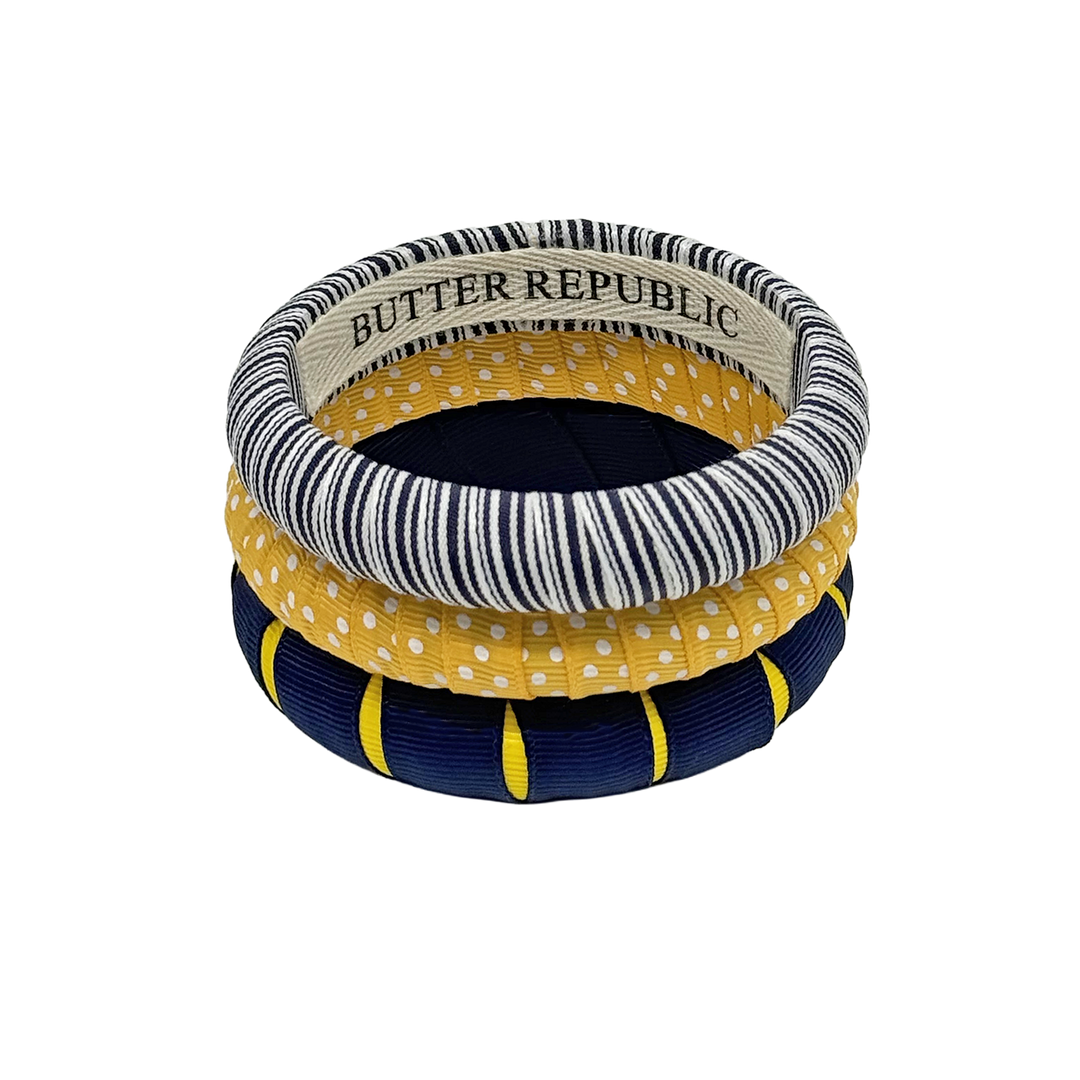 A stack of three assorted designs of navy blue and yellow Butter Republic bracelets