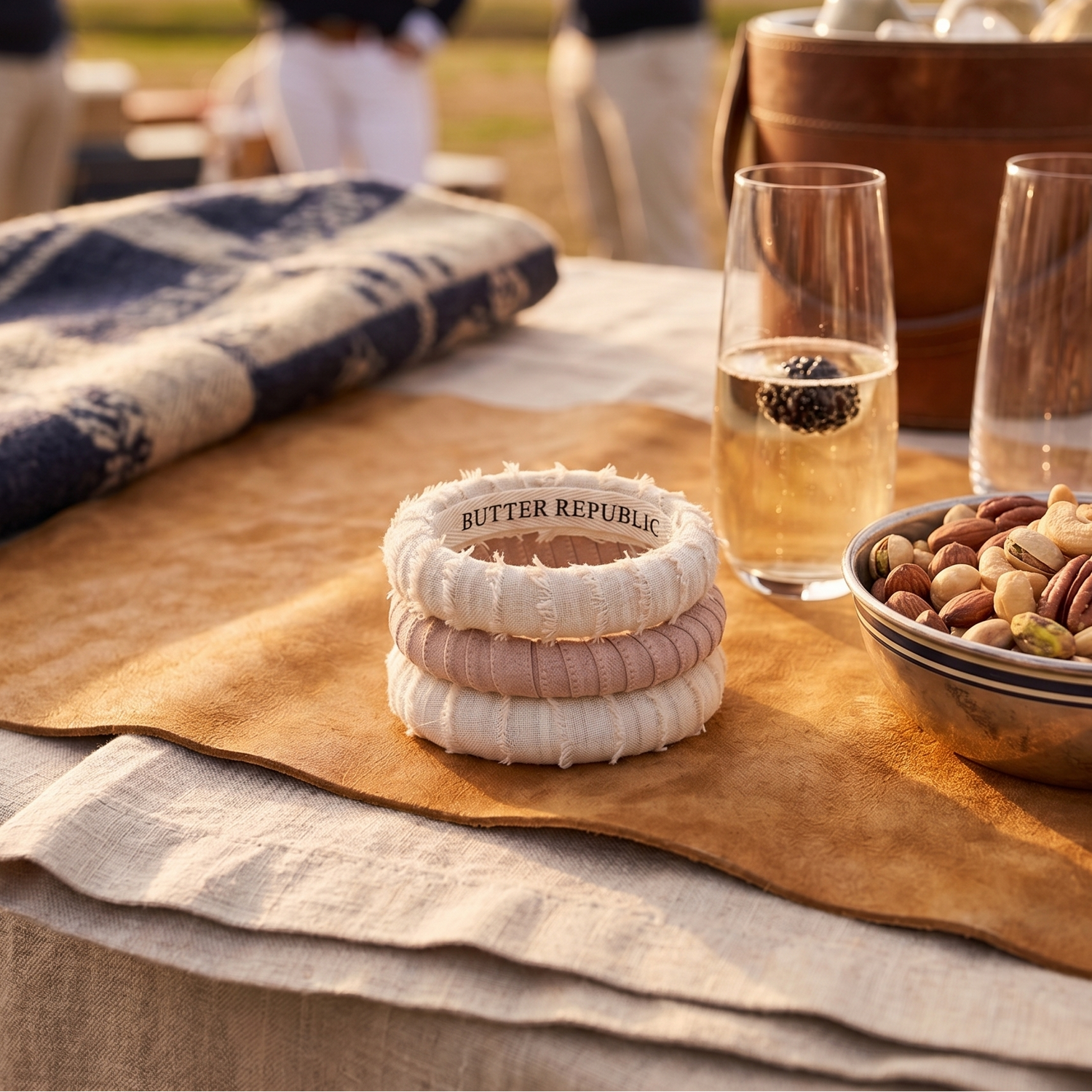 stack of three frayed Butter Republic bracelets on a table with glasses and snacks outdoors