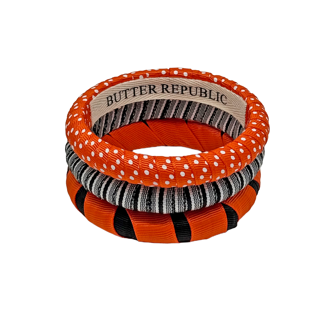 A stack of three orange and black Butter Republic bracelets