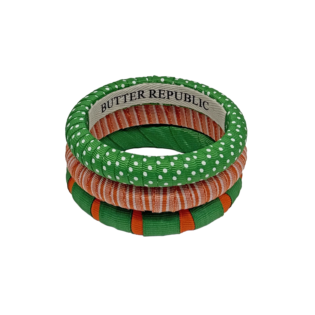 Three stacked assorted designs of Butter Republic orange, green, and white bangle bracelets
