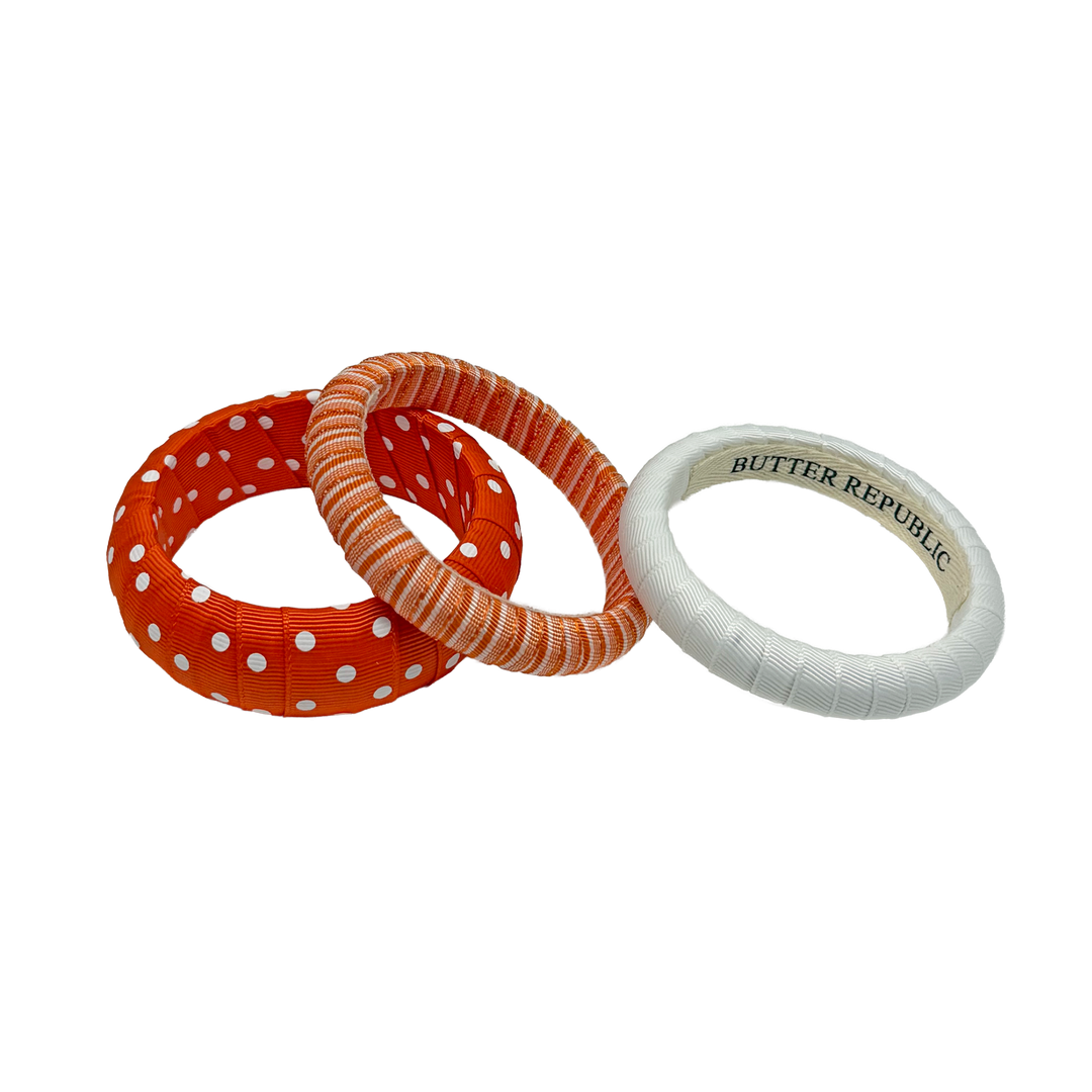 Three assorted orange and white Butter Republic bracelets with brand label on the interior