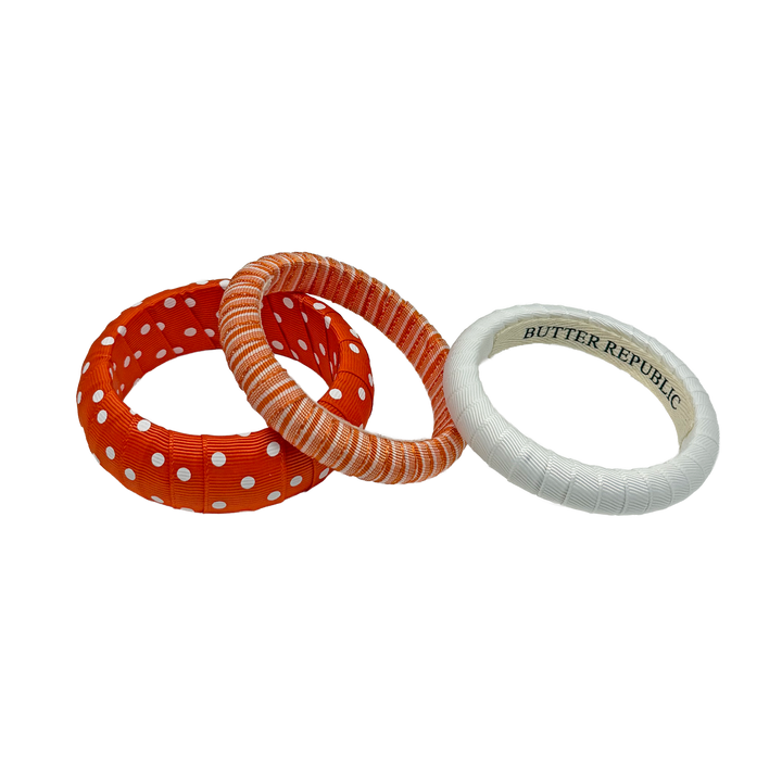 Three assorted orange and white Butter Republic bracelets with brand label on the interior
