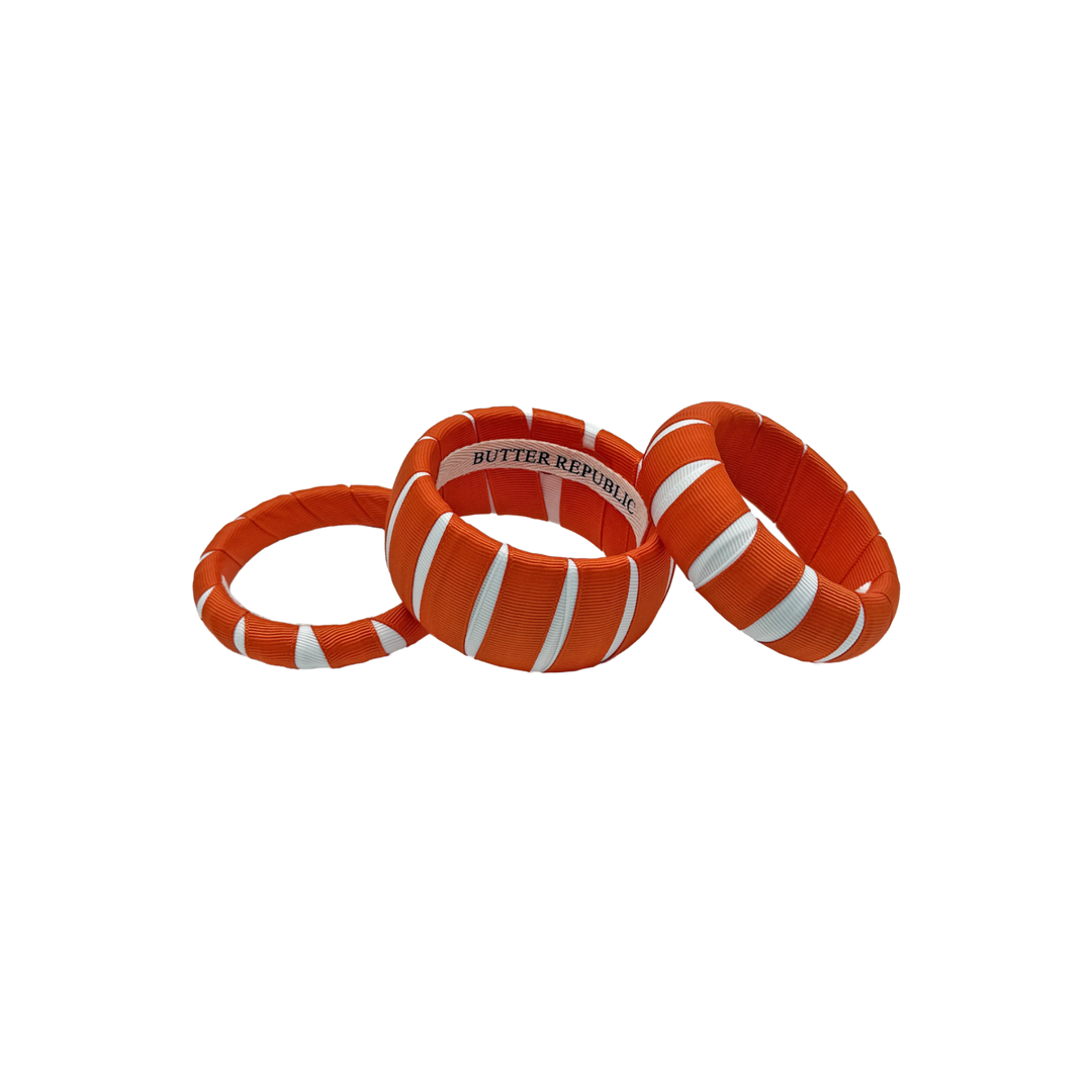 three multi-width orange and white Butter Republic bracelets with a logo brand label on the interior of the bracelet
