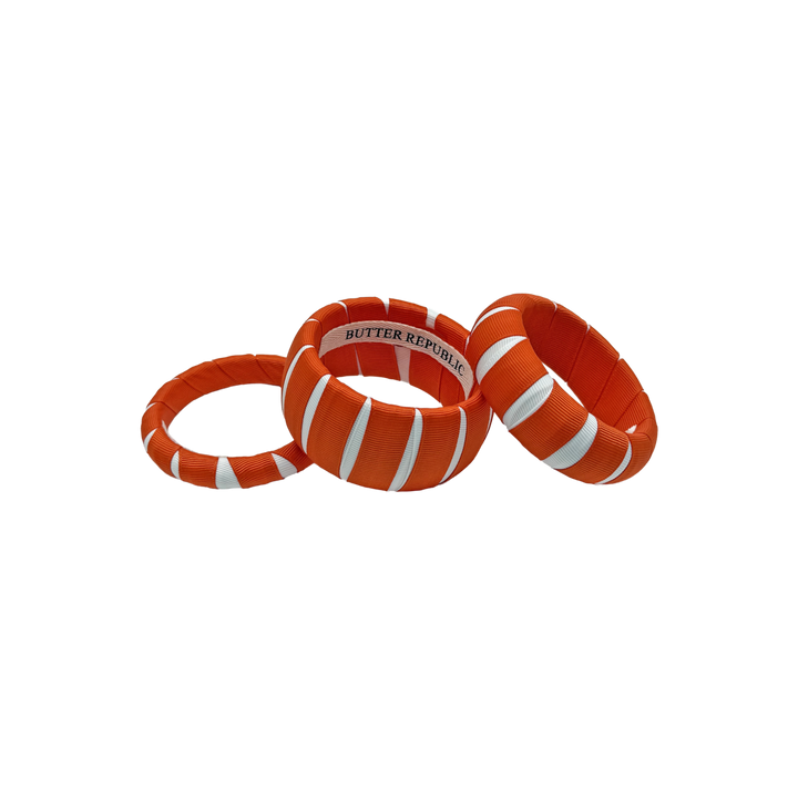 three multi-width orange and white Butter Republic bracelets with a logo brand label on the interior of the bracelet