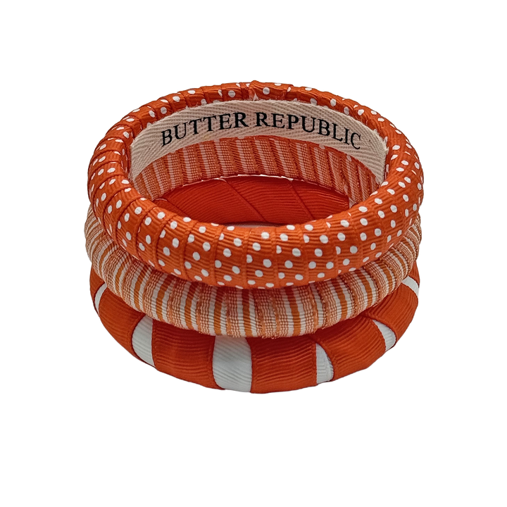 stack of three orange and white narrow Butter Republic bracelets with logo brand label on the interior of the bracelet