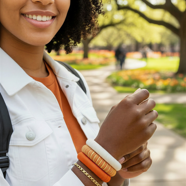 Woman wearing multiple burnt orange and white bangle bracelets outdoors in a campus setting