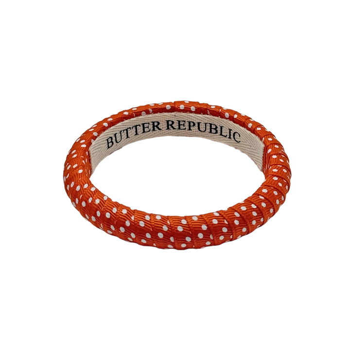 orange and white swiss dot Butter Republic bracelet with a brand label on the interior of the bracelet
