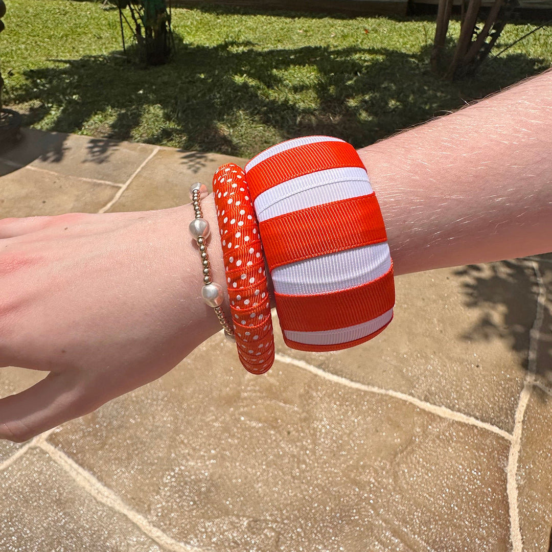 Woman wearing two orange and white Butter Republic bracelets on a stone patio with grass and plants in the background