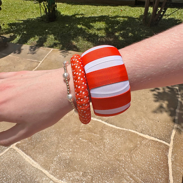 Woman wearing two orange and white Butter Republic bracelets on a stone patio with grass and plants in the background