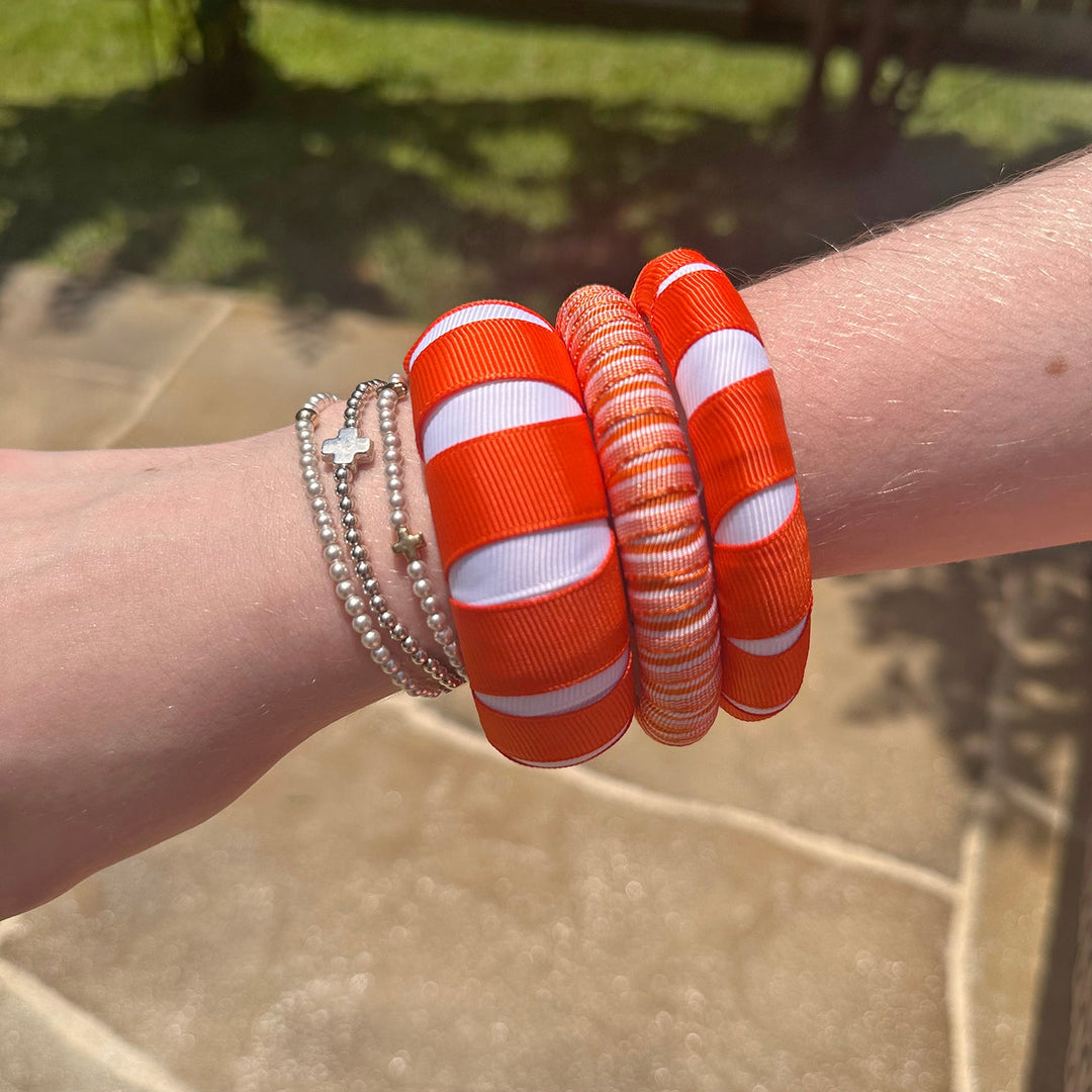 Woman wearing three orange and white Butter Republic bracelets on a stone pavement background