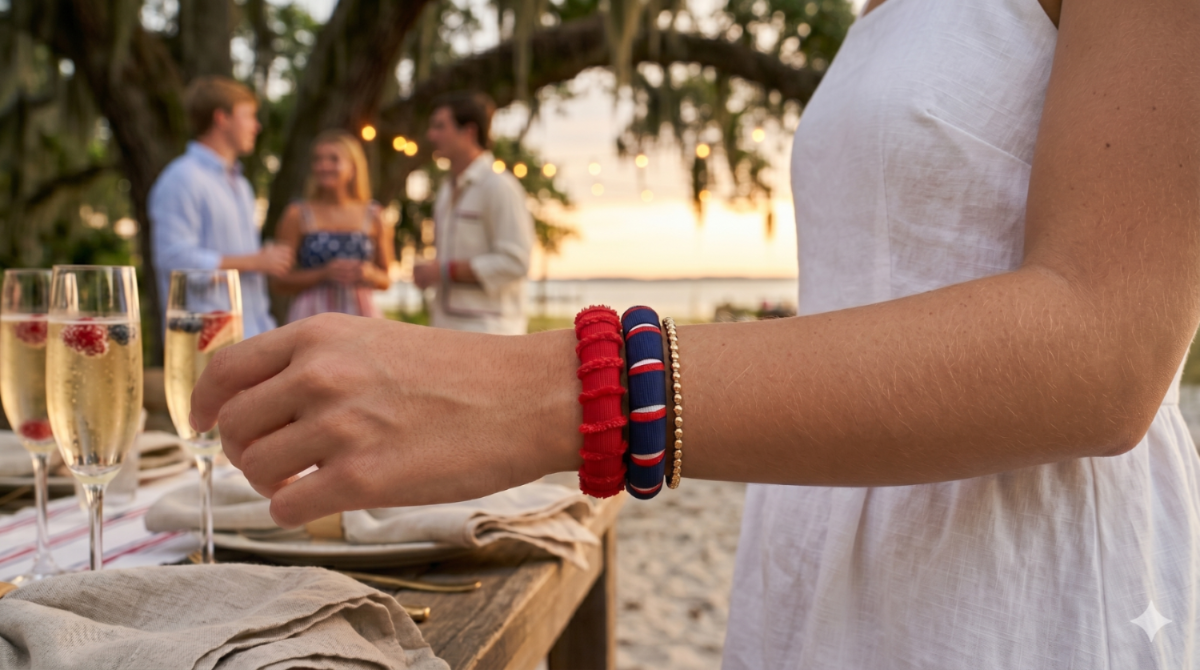 young woman wearing a red, white, and blue Butter Republic bracelet with a brand label on the interior of the bracelet, at an outdoor dining table with friends in the background