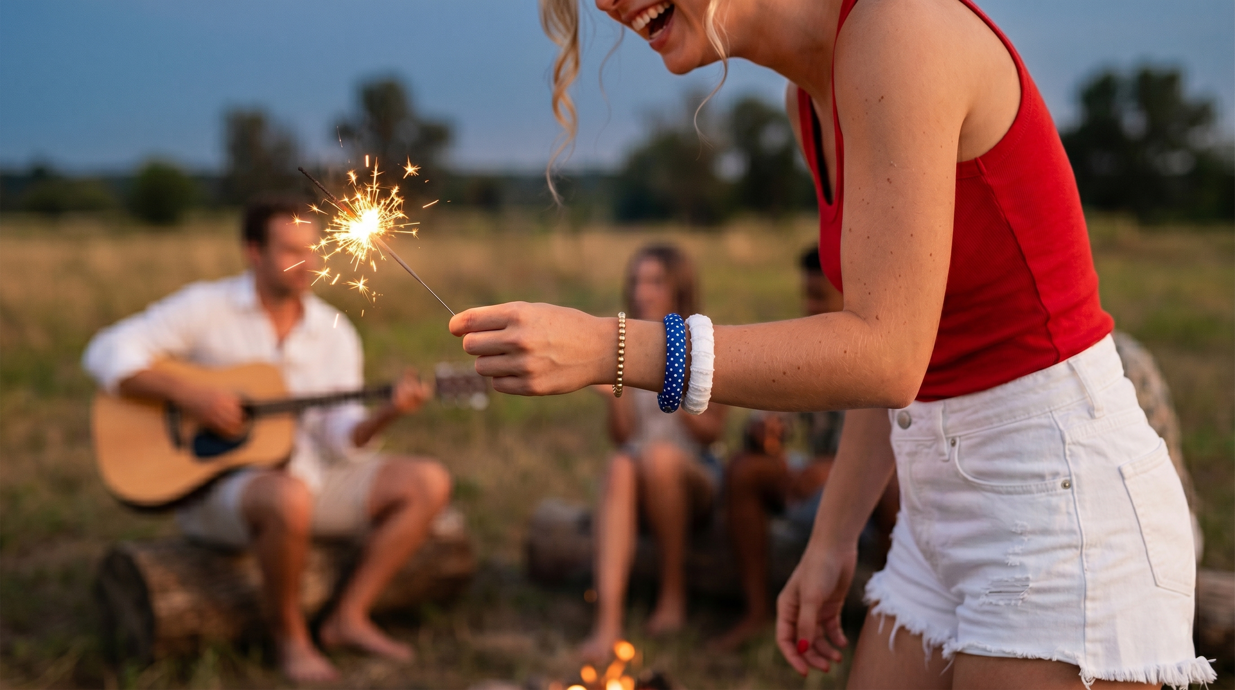 woman wearing a blue and white Butter Republic bracelet and a white Butter Republic bracelet, holding a sparkler with people playing guitar in the background