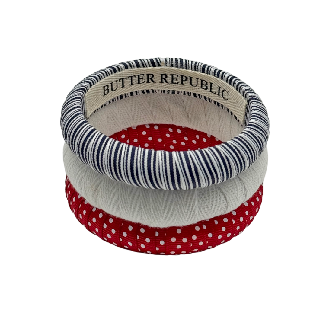 three Butter Republic bracelets with a brand label on the interior of each bracelet with patriotic colored patterns stacked