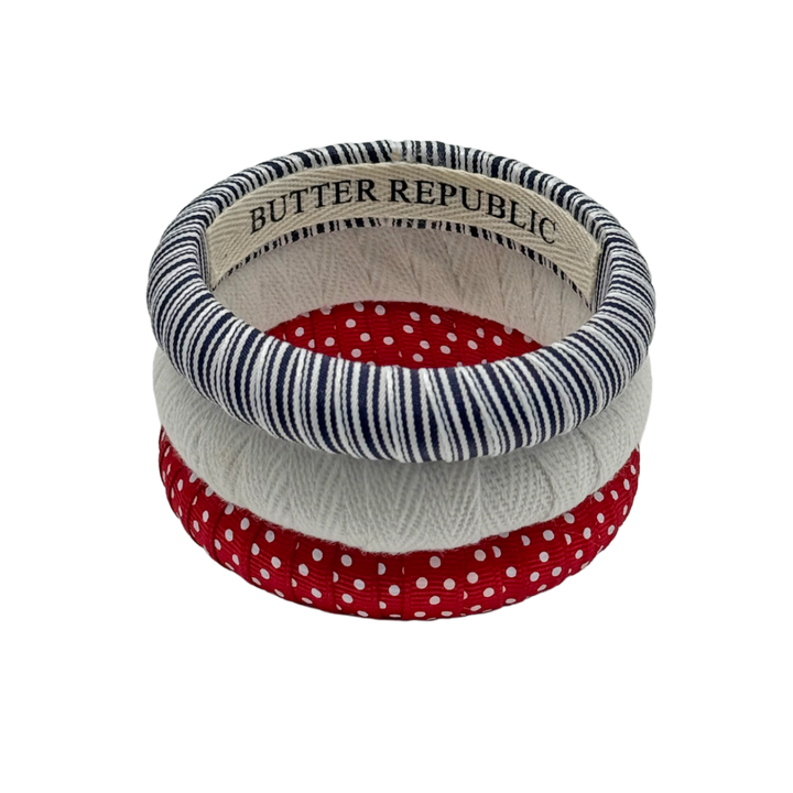 three Butter Republic bracelets with a brand label on the interior of each bracelet with patriotic colored patterns stacked