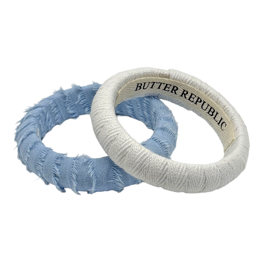 two Butter Republic bracelets with a brand label on the interior of each bracelet, one powder blue Butter Republic bracelet and one white Butter Republic bracelet
